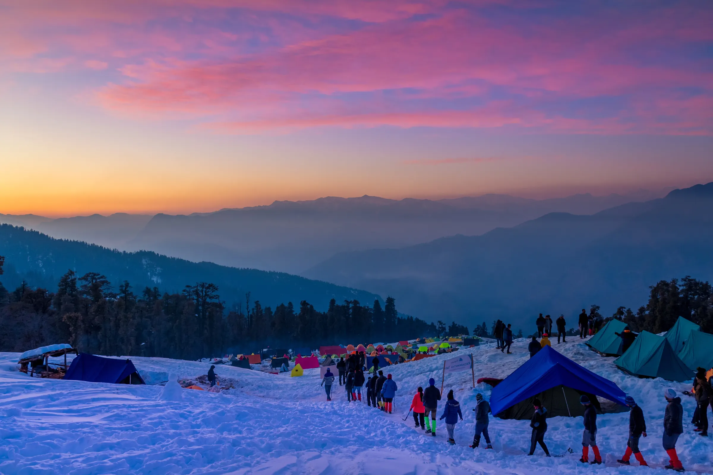 A managed camp on the Kedarkantha trek at first light, tents pitched and groups moving out
